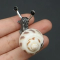 Detalle de broche de caracol con concha natural y textura de metal plateado fino - Broche de Caracol Plateado con Concha Moteada