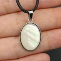 Colgante ovalado de nácar con marco plateado y cordón negro sujeto en la mano - Colgante con Cordón / Collar de Nácar Blanco