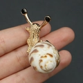 Broche de caracol dorado con textura de concha natural y detalles de piedras negras - Broche de Caracol Dorado con Concha Moteada