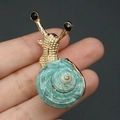 Broche escargot avec coquille en spirale verte et finition en métal doré sur la main - Broche Escargot Dorée à Coquille Verte