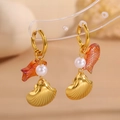 Dettaglio macro di orecchini dorati con perla, ciondolo a pesce e pendente a conchiglia - Stile Pendente Conchiglia Pesce Koi