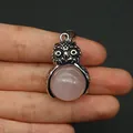 Dettaglio ravvicinato di un ciondolo a gufo in argento con pietra rosa tra le dita - Quarzo rosa