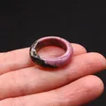 Polished pink rhodonite natural stone ring with black mineral textures on black background - Rhodonite