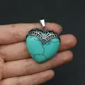 Hand hält Herz-Anhänger aus Türkis mit silberner filigraner Metallfassung im Vintage-Stil - Blauer Türkis