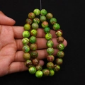 Macro detail of round green emperor stone beads held by hand for DIY jewelry making - Green Brown Textured (No. 5)