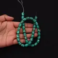 Dettaglio ravvicinato di perle cilindriche in turchese verde tenute come riferimento - 8X10mm / Verde Pavone Venato (N. 12)