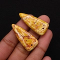Macro detail of triangle natural stone pendants in yellow with reddish veins held in hand - 15x34mm
