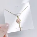 Nahaufnahme einer goldenen Schlüsselkette mit rosa Blütenblättern und funkelnden Kristallen - Rosa Blumen-Schlüssel-Stil