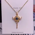 Macro shot of gold key pendant with crystal wings and projection stone on necklace - Key Wand Style (TY0056) / Gold