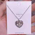 Detalle del collar MOM con forma de corazón plateado y cristales en tarjeta blanca - Corazón Doble M Plateado (MOM14)