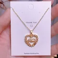 Detalle de un colgante de corazón dorado con letras Mom y un pequeño cristal en la cadena - Piedra de Corazón Único Dorada (MOM01)