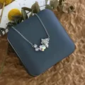 Détail du pendentif trèfle argenté avec breloque chat sur écrin et eucalyptus - Chat Trèfle Cristal Argent (XL0606)