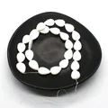 Macro detail of white leaf-shaped shell beads with fine carved texture on a dark tray - Leaf Shape