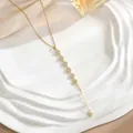 Macro detail of golden Y-shaped tassel necklace with micro-pave zircons on ceramic tray - Seven Pave Round Element Style (XL01925)