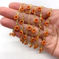 Cadena dorada con dijes de esmalte naranja vibrante sostenidos en la mano - Rojo Anaranjado