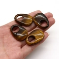 Macro shot of four natural tiger eye stone teardrop charms held in a hand - Tiger's Eye