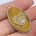 Tijgeroog ovale hanger met hart filigraan in roségouden frame in de hand gehouden - Tijgeroog Hartpatroon