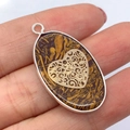 Ovale stenen hanger met gouden hart overlay en zilveren rand vastgehouden in hand - Gouden Zijde Jade Hartpatroon