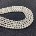 Close-up of natural freshwater rice pearls with high luster on a black texture base - 3-4mm / White