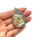 Détail d'un pendentif goutte en nacre d'abalone avec bordure en strass étincelants en main - Ovale / 20x56mm