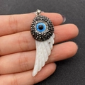 Natural shell wing pendant with evil eye design and rhinestones held in fingers - Evil Eye Wing Shape / 19x52mm