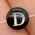 Macro view of a black round shell bead featuring a gold letter D for DIY jewelry making - Letter D / 8mm