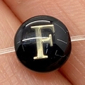 Macro view of a black shell bead featuring a golden letter F for DIY jewelry - Letter F / 8mm