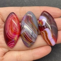 Three marquise-cut dragon vein agate beads in red, grey, and purple held by a hand - No.7 (Purple Banded Agate)