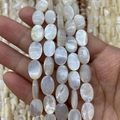 Macro detail of oval white mother of pearl loose beads with iridescent luster on hand - Flat Oval Style (No. 1) / 8X12mm