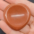 Pierre de pouce en goldstone orange en forme de cœur tenue dans la main - 40x40x6mm / Pierre de Sable d'Or
