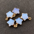 Vue détaillée de cinq pendentifs étoiles facettés avec bordures dorées sur fond gris - 13x16mm / Opale