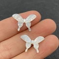 Makrodetail eines Schmetterlingsanhängers aus Naturmuschel mit Perlglanz auf Fingerspitzen - Weiße Schale, 18x20mm