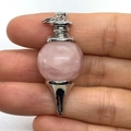 Pink quartz crystal ball pendant with silver metal base shown between fingers - 18x41mm / Rose Quartz