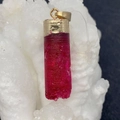 Close-up of cylindrical ruby red natural stone pendant with gold metal cap and texture - Purple Crystal