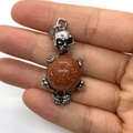 Gothic skull pendant holding a brown goldstone sphere with a silver metal pinch bail - Gold Sandstone