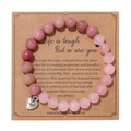 Detalle de pulsera de piedra cebra rosa con dije de corazón en tarjeta de regalo - Cuarzo Rosa Con Madera Roja