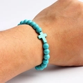 Detailed view of a turquoise beaded bracelet with a cross charm on a person's wrist - Teal Round Beads With Cross (08)