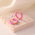 Macro detail of pink enamel hoop earrings on a textured stone stand with soft wavy fabric - Rose Red