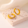 Macro detail of glossy yellow enamel gold hoop earrings on beige stone base - Orange