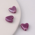 Makroaufnahme lila Keramik-Herzperlen mit glänzender Glasur und Bohrung für DIY-Schmuck - Dunkellila