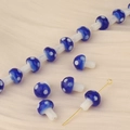 Macro detail of blue glass mushroom beads with white polka dots on beige silk fabric - Sapphire Blue