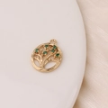 Close-up of gold plated tree of life pendant with green zircon stones on silk fabric - Green Tree Of Life