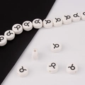 Close-up of white ceramic Taurus zodiac beads showing the black symbol and threading holes - Taurus