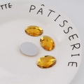 Macro detail of amber yellow oval flatback acrylic rhinestones on a decorative white plate - Standard Spec / Gold Yellow