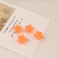 Macro detail of four translucent orange acrylic star charms with silver metal rings - Orange