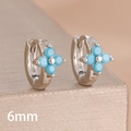 Close-up of 6mm silver four-leaf clover earrings with blue zircon stones on a gold stand - 6mm-Silver Blue-1 Pair