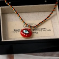 Detail of multi-color woven rope necklace with red enamel evil eye charm on display card - Evil Eye Style / Red