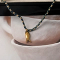 Macro shot of gold fish pendant on blue and gold braided rope necklace for jewelry lovers - Fish Style / Blue and Gold Woven