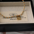 Detail of colorful braided cord bracelet with gold square Good Luck charm on black box - Good Luck Square Plate Style (good luck) / Multicolor Woven