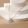 Close-up of gold pear-cut blue zircon teardrop pendant with shiny water-drop stone - December Blue Zircon